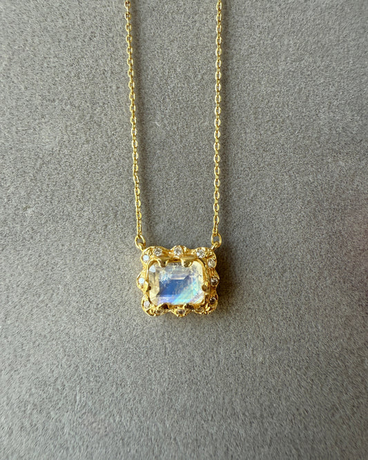 Gold necklace with a blue and rainbow gemstone pendant on a gray background