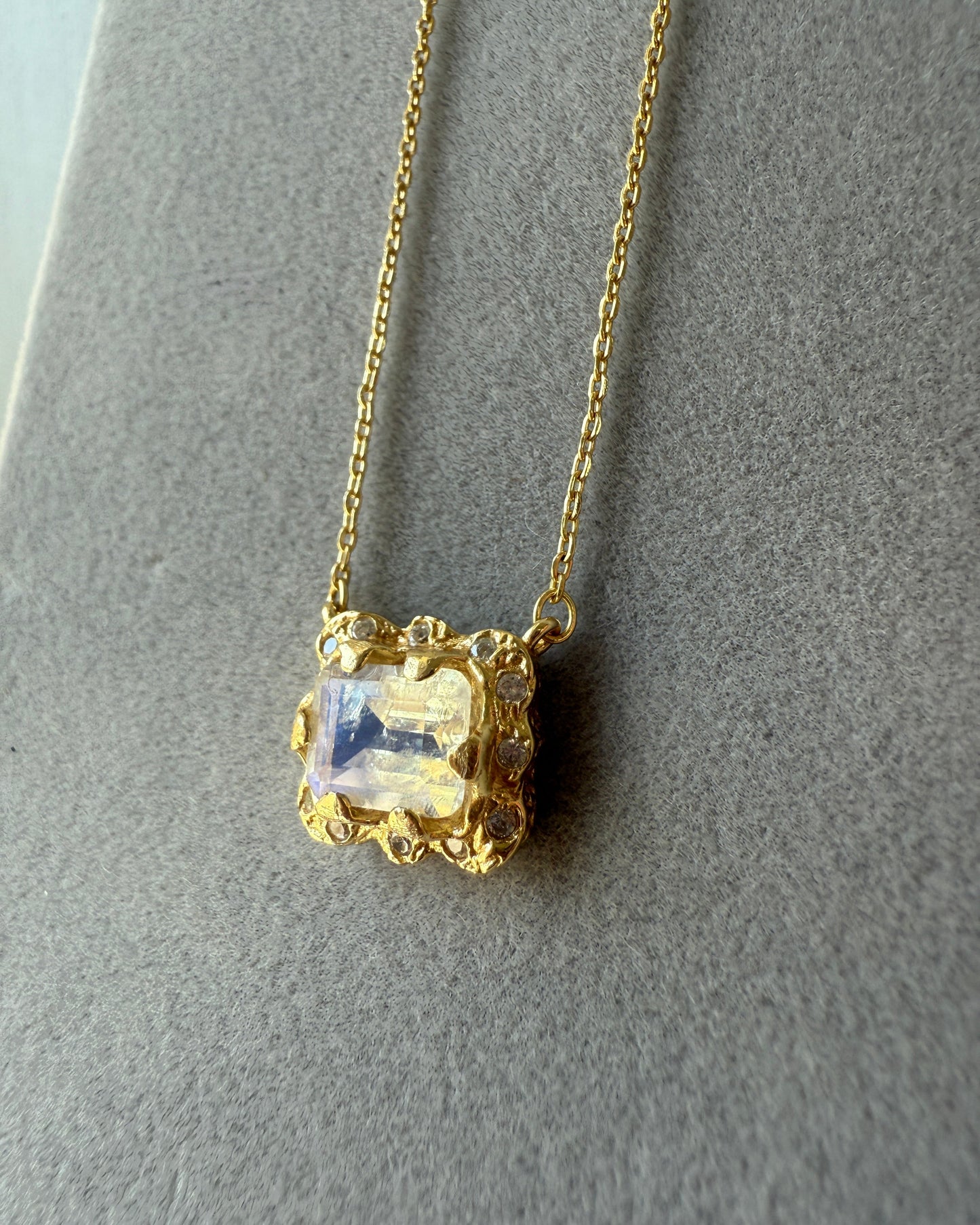 Gold necklace with a clear gemstone on a gray background