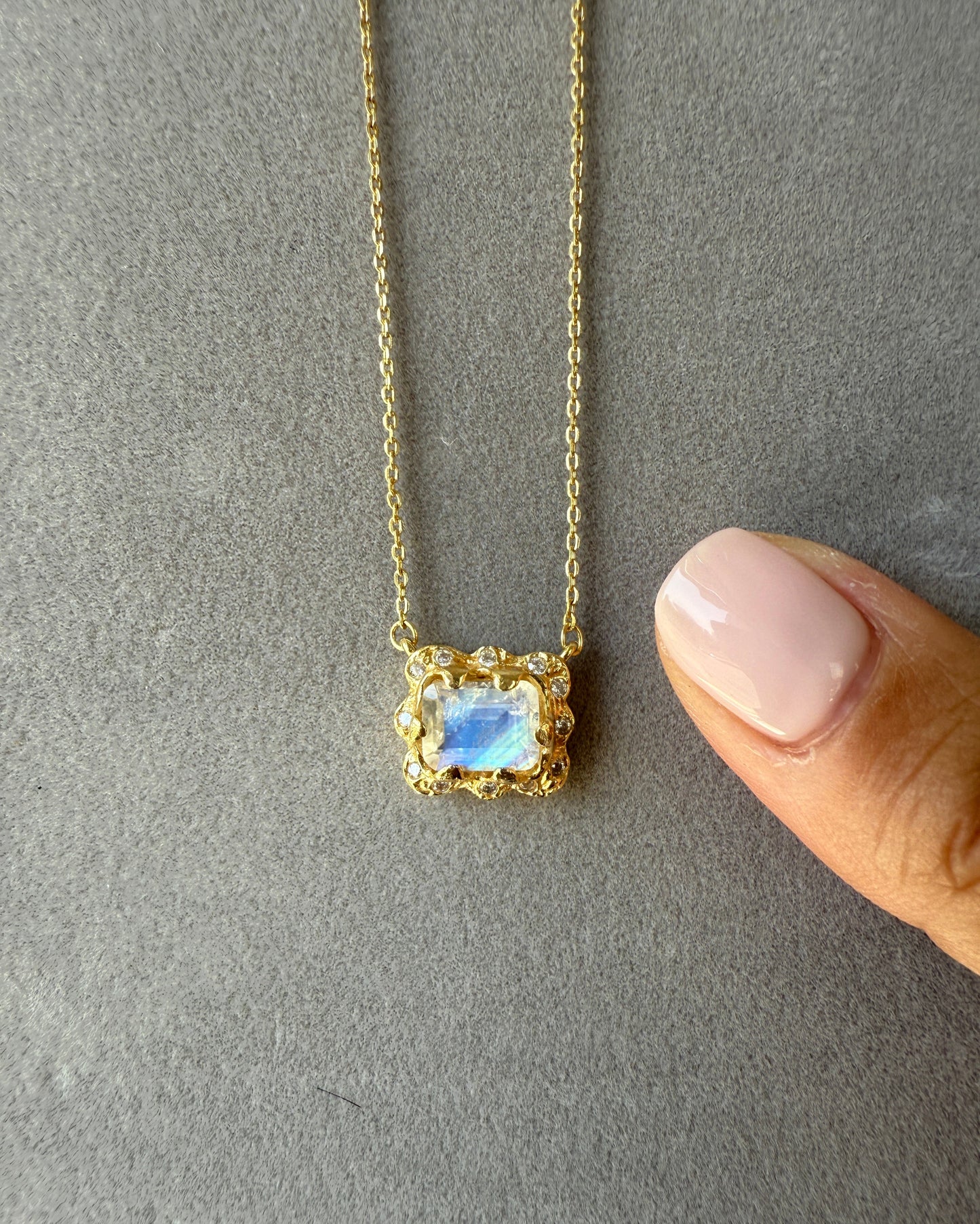 Gold necklace with a blue gemstone pendant on a gray surface.